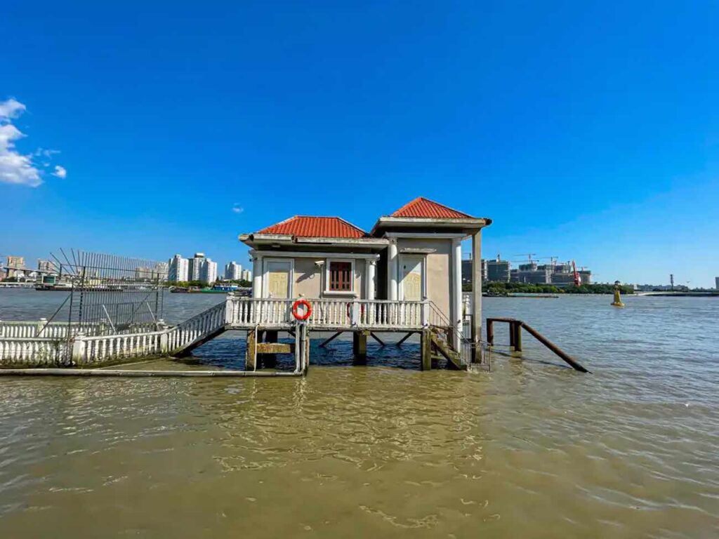 57 things to do in shanghai: the ultimate handbook 23 things to do in shanghai "a small traditional building with red roofs is partially submerged in floodwaters at a shanghai water town, surrounded by railings on a sunny day with an unbelievable modern cityscape in the background—showing unique day trip things to do in shanghai beyond the city center.
