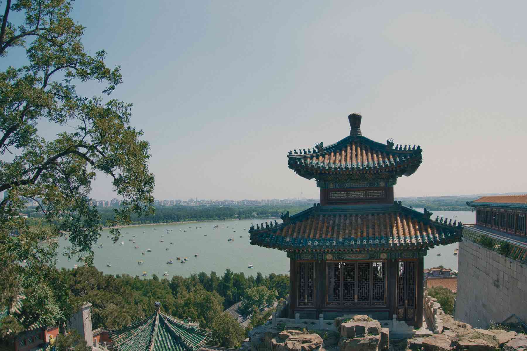 Het traditionele Chinese paviljoen met sierlijke daken kijkt uit over een uitgestrekt meer met boten en een vergezicht over de stad aan de horizon, omgeven door weelderig groen en bomen. Een ideale omgeving voor het opbouwen van zakelijke relaties in China.