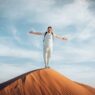 De ultieme gids voor de woestijn in Oman: Wahiba Sands 28 Wonen als expat in Erbil Een persoon staat op de voorgrond van een enorme zandduin en omarmt met uitgestrekte armen de elementen onder een bewolkte lucht.