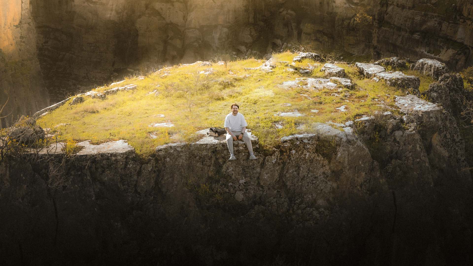 A person sitting on a rocky outcrop, overlooking a deep canyon, surrounded by sunlight and grassy terrain, prominently featured on the front page designed with Elementor.