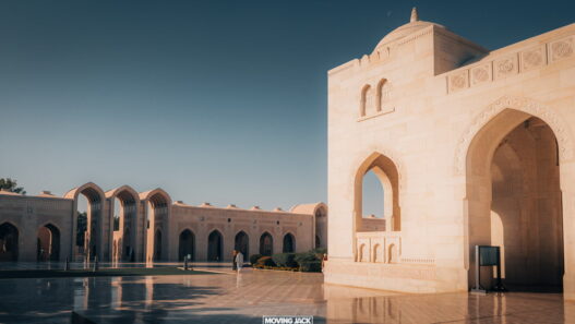 A sunlit courtyard featuring traditional arched architecture under a clear sky invites you to explore, raising the question: how many days to spend in oman to truly savor its beauty?