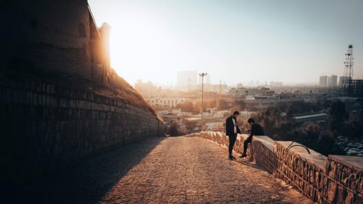 21 unique things to do in erbil 19 Two people sit on a stone wall along a sloping cobblestone path, overlooking erbil's cityscape at sunset, enjoying one of the top things to do in this vibrant destination.