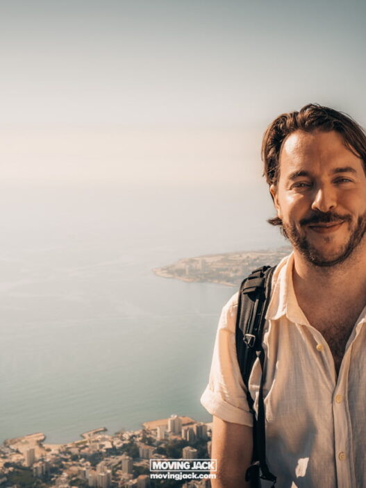 12 expert tips for traveling without knowing the local language 27 travelling with cats A person with a backpack smiles in front of a scenic coastal view under a clear sky.