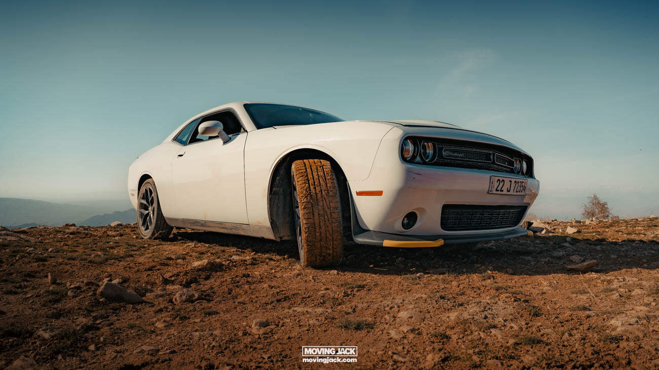 White sports car parked on a dusty terrain in erbil with a clear sky in the background.