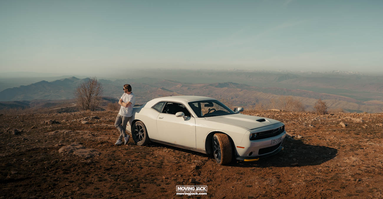 Visiting erbil & iraq for the first time: expert guide + tips 12 first time A first-timer stands next to a white dodge challenger parked on a rocky hilltop, taking in the vast mountain and valley views. -copyright-moving-jack. Com