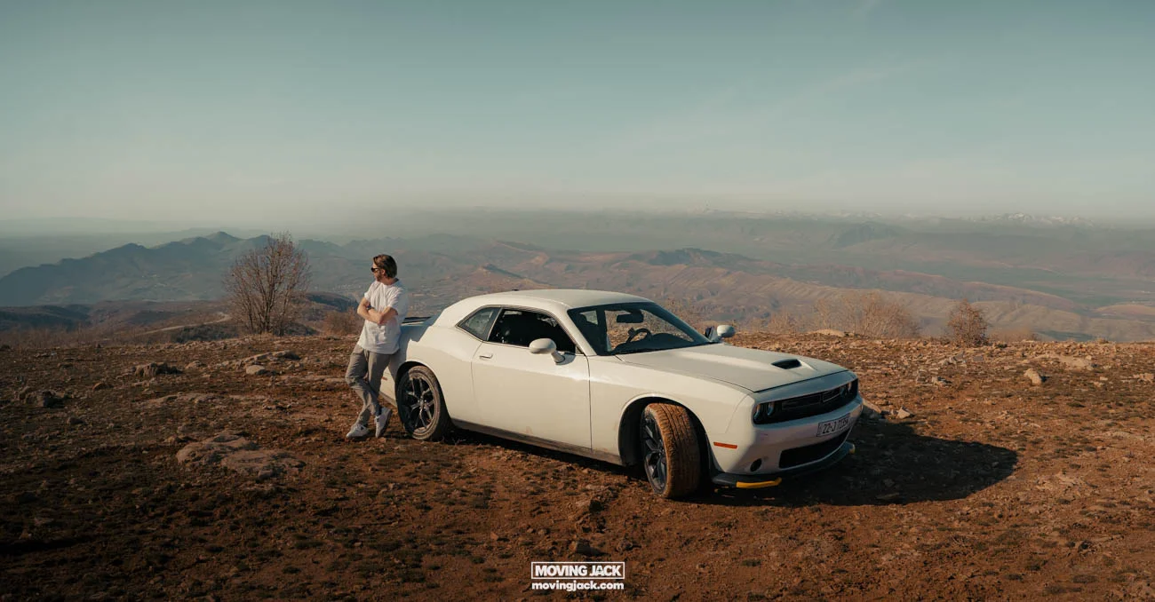 Visiting erbil & iraq for the first time: expert guide + tips 11 first time A first-timer stands next to a white dodge challenger parked on a rocky hilltop, taking in the vast mountain and valley views. -copyright-moving-jack. Com