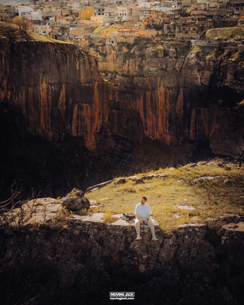 About moving jack 7 about me Man sitting on a rock ledge with a dramatic view of a deep gorge and densely packed houses on the opposite cliff, captured through the lens of a tamron 50-400.