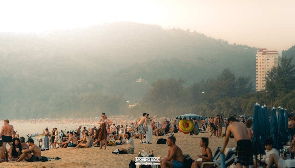 Een bruisend strand waar zonaanbidders ontspannen en genieten van talloze activiteiten, omlijst door weelderige heuvels en torenhoge wolkenkrabbers - een momentopname van waarom Phuket bezoeken voor een onvergetelijke tropische ontsnapping. -copyright-moving-jack. Com