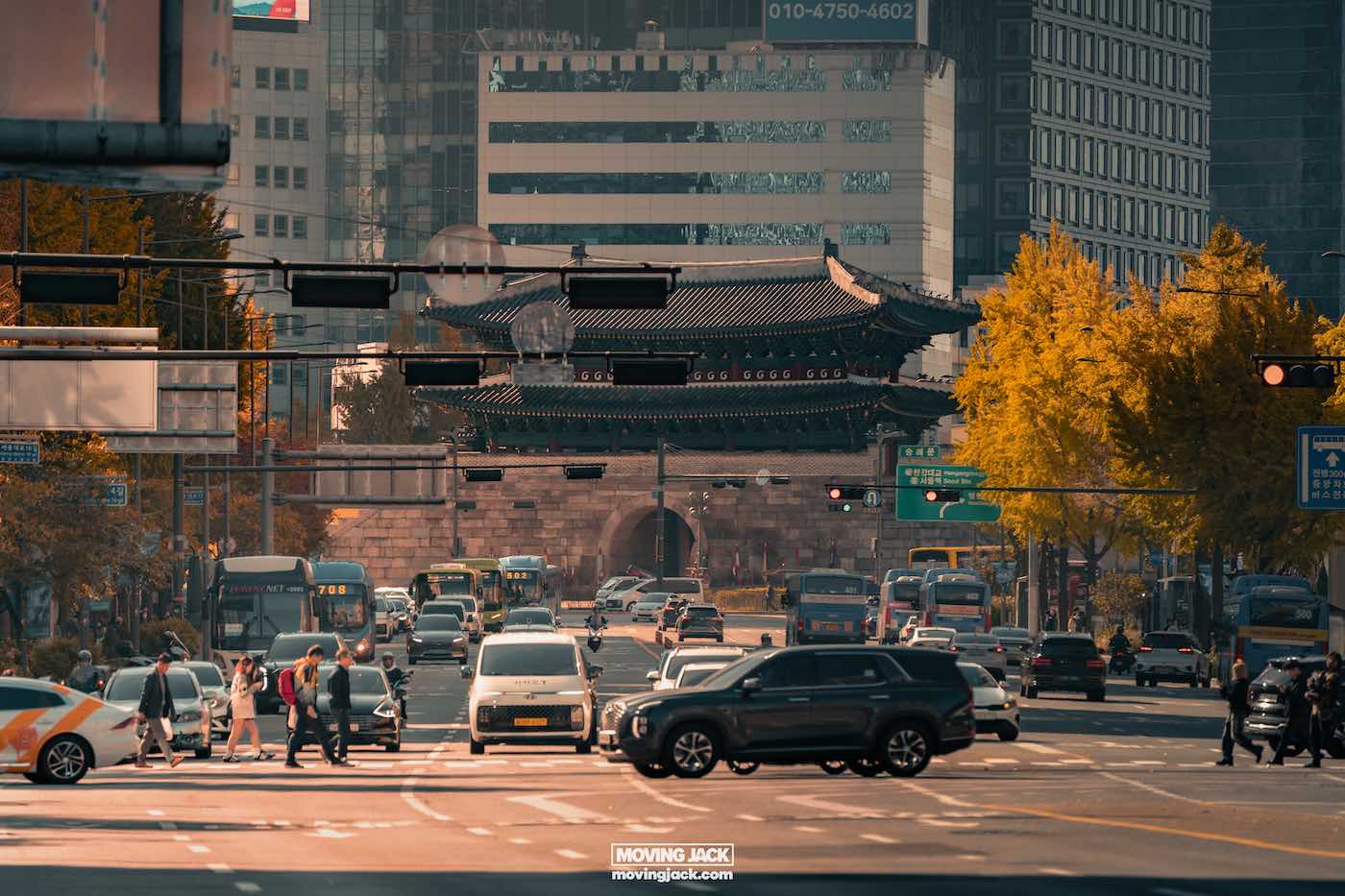 Amidst the hustle of a busy city street, where cars and pedestrians fill the autumn air, a historic gate stands gracefully against a backdrop of modern buildings. It's a scene that might leave you pondering where to stay in seoul to capture such vivid urban contrasts. -copyright-moving-jack. Com