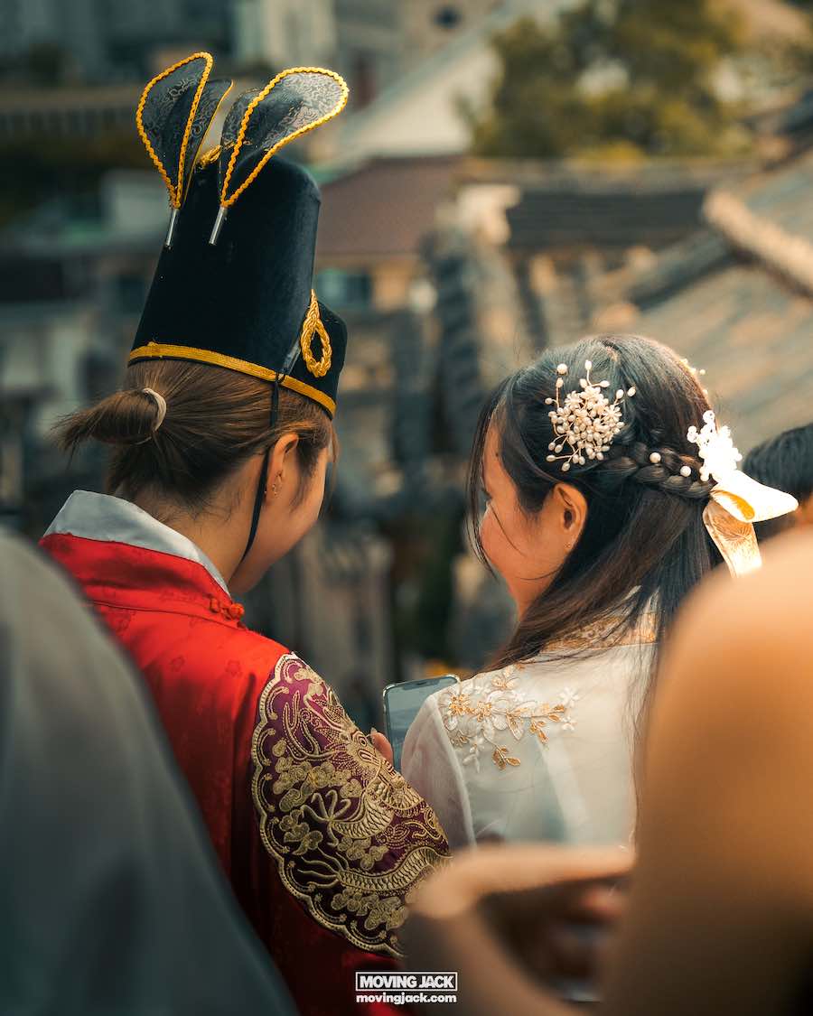 Waar te verblijven in Seoul: beste hotels + reisgids voor gebieden 13 waar te verblijven in Seoul Twee mensen in traditionele kledij worden van achteren gezien; de een draagt een sierlijke hoed en een rood gewaad, de ander heeft bloemenhaaraccessoires en een wit topje. Ze lijken deel te nemen aan een buitenevenement, wat misschien een glimp geeft van culturele gebruiken die bezoekers kunnen verkennen als ze overwegen waar ze in Seoul willen verblijven. -copyright-moving-jack. Com