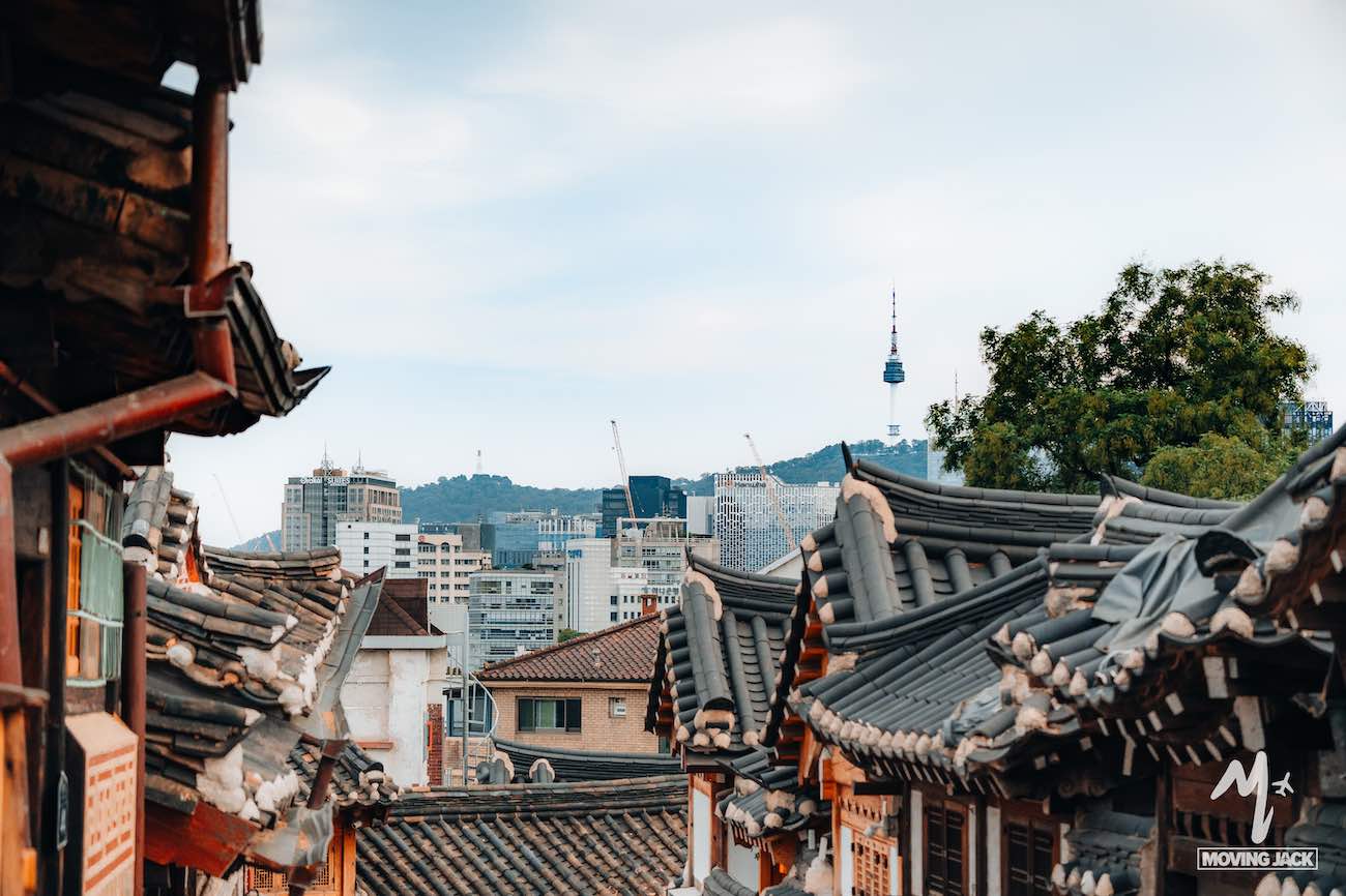 Traditionele Koreaanse daken in Bukchon Hanok Village, een van de beste buurten om te verblijven in Seoul, met op de achtergrond moderne gebouwen en de Namsan-toren.