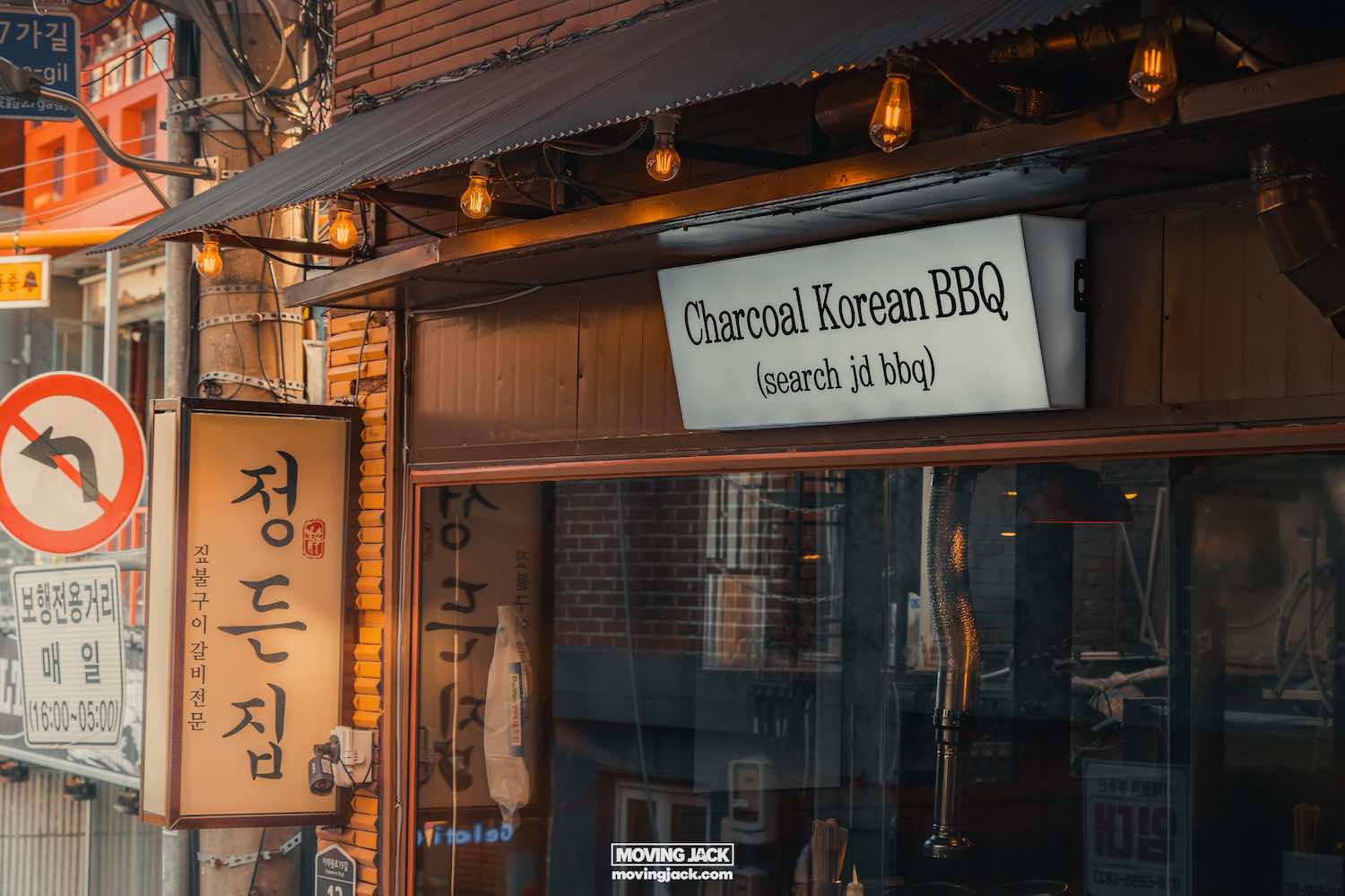 Reisroute Itaewon 2025: de beste eetgelegenheden, drankjes en uitgaansgelegenheden 6 Itaewon Straatbeeld van een Koreaans bbq-restaurant in Itaewon met een bord met de tekst "houtskool Koreaanse bbq". Binnen is warme verlichting zichtbaar en er hangen gloeilampen onder de luifel. -copyright-moving-jack. Com