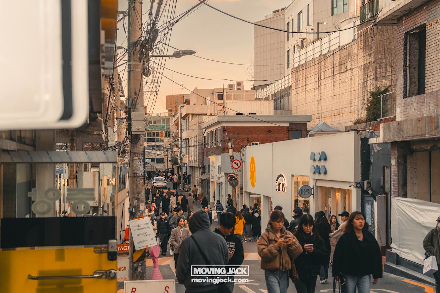 Reisroute Itaewon 2025: de beste eetgelegenheden, drankjes en uitgaansgelegenheden 19 Itaewon Een bruisende stedelijke straatscène in Itaewon met mensen die langs een smalle weg lopen, geflankeerd door levendige winkels en gebouwen onder een bewolkte hemel. -copyright-moving-jack.com