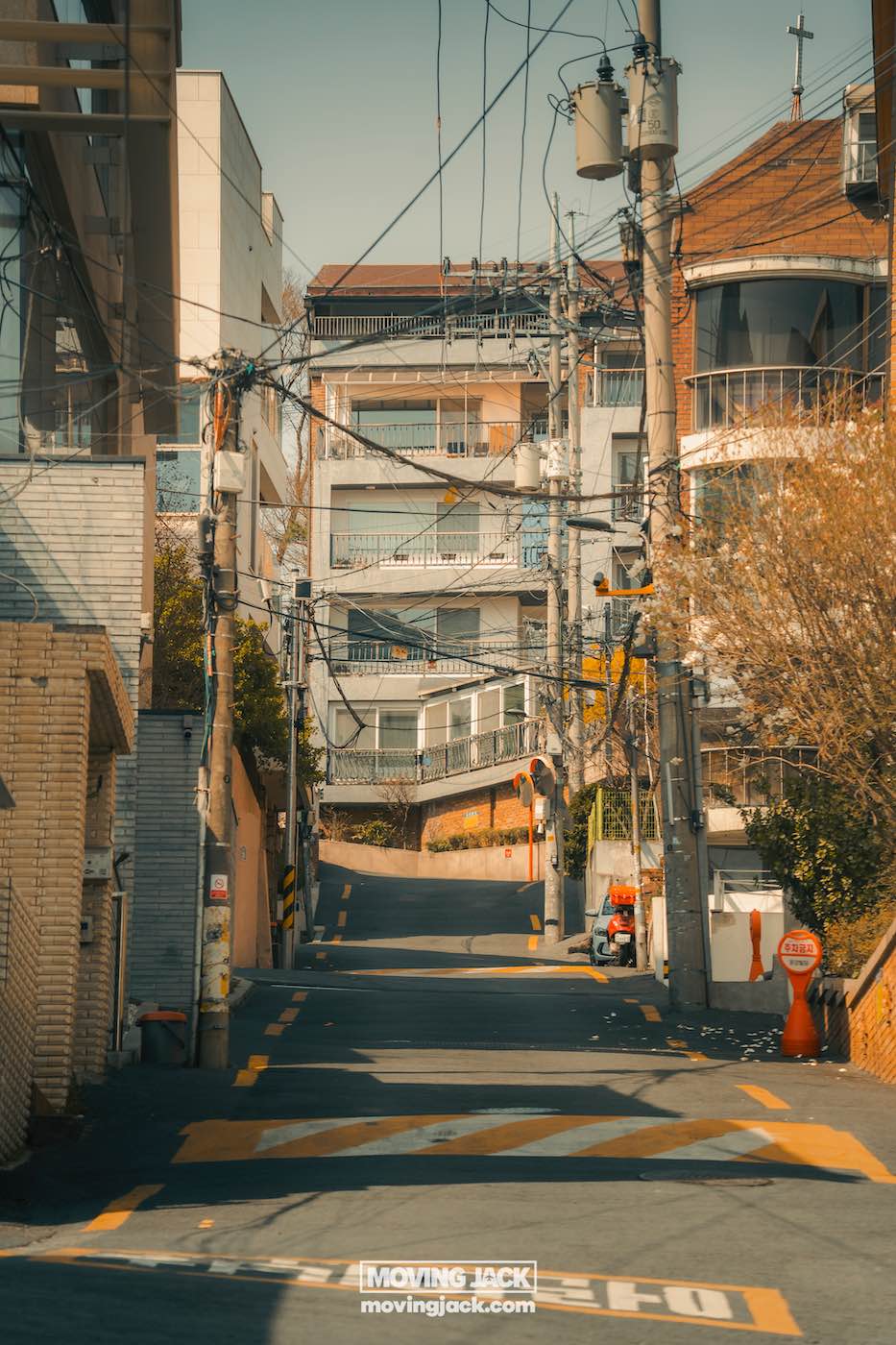 Reisroute Itaewon 2025: de beste eetgelegenheden, drankjes en uitgaansgelegenheden 36 Itaewon Smalle straat in Itaewon, bezaaid met gebouwen, elektriciteitspalen en bovenleidingen onder een heldere hemel. Oranje kegels markeren de lopende wegwerkzaamheden. -copyright-moving-jack.com