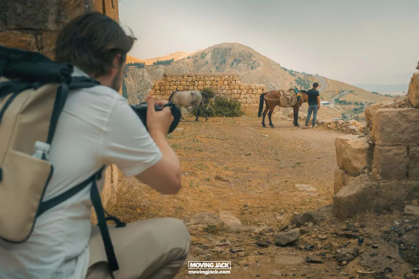 Visiting erbil & iraq for the first time: expert guide + tips 16 first time A person with a backpack captures photos of two first-timers with horses near stone ruins in a hilly landscape. -copyright-moving-jack. Com