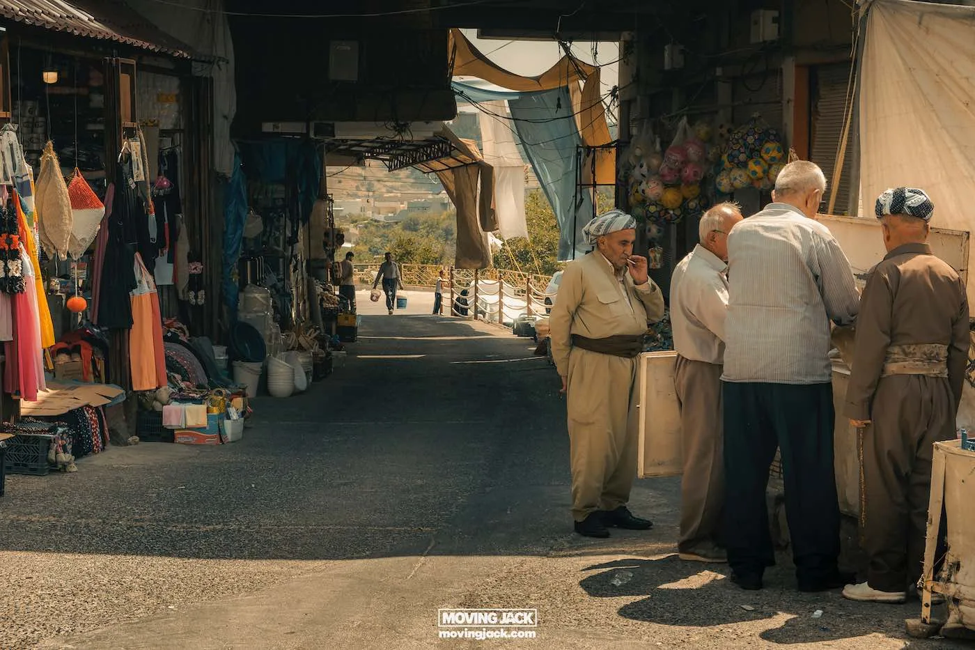 Visiting erbil & iraq for the first time: expert guide + tips 8 first time A group of men in traditional attire stand and converse near a market stall under a covered passageway, offering a rich experience for first-timers exploring the vibrant array of goods, as a person walks by in the distance. -copyright-moving-jack. Com