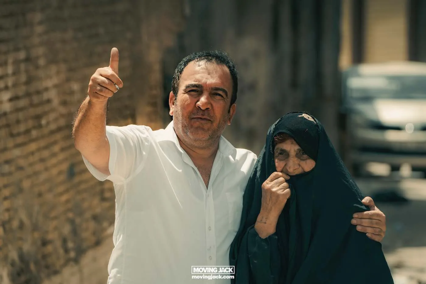 Visiting erbil & iraq for the first time: expert guide + tips 15 first time A man in a white shirt gives a thumbs up beside an older woman in a dark headscarf on a sunlit street, suggesting it's their first time exploring the bustling neighborhood together. -copyright-moving-jack. Com