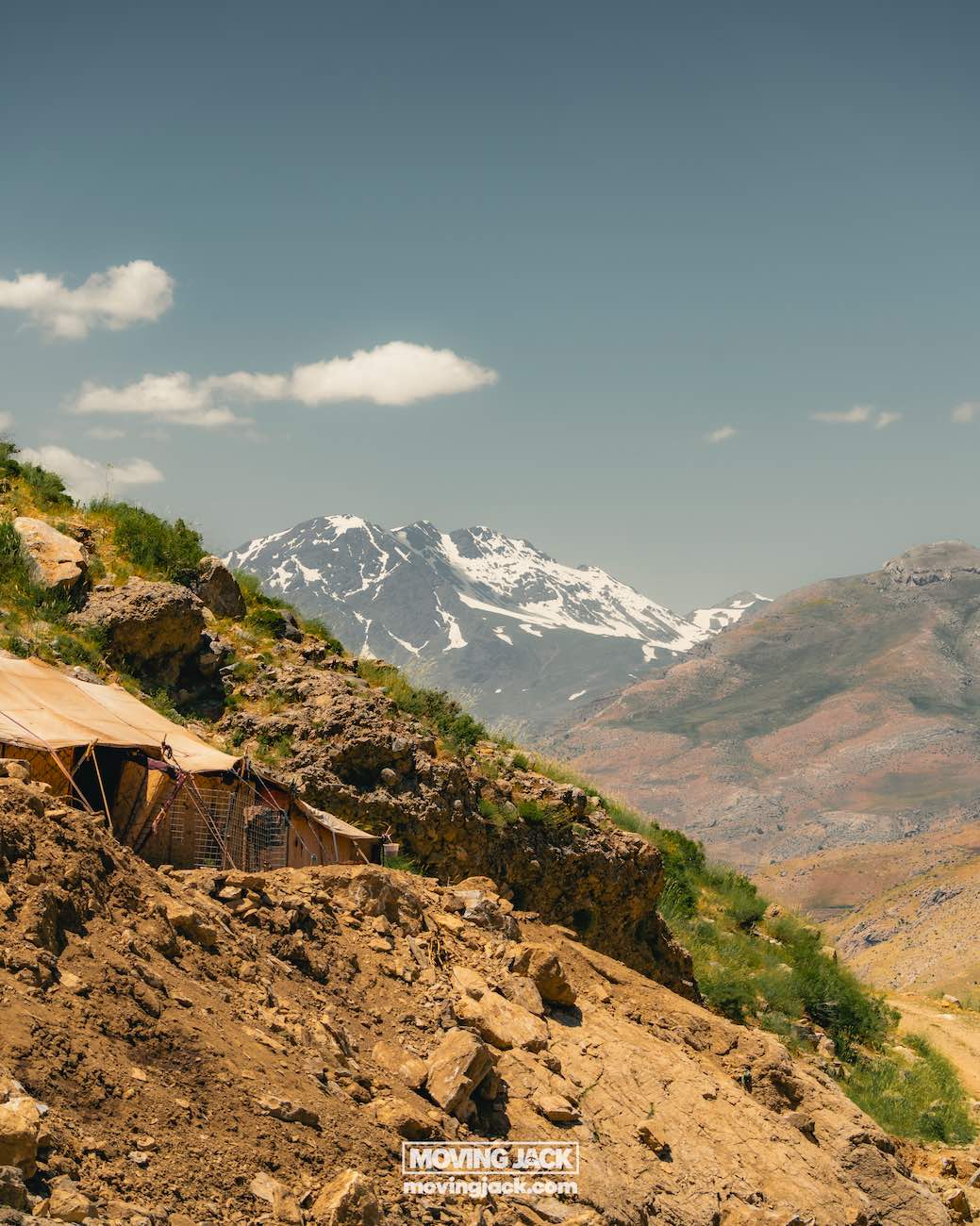 De majestueuze bergen en natuur van Koerdistan - wandelavontuur (Irak) 18 Koerdistan, wandelen in Koerdistan, wandelen in de bergen van Koerdistan, de natuur van Koerdistan Een ruige berghelling met een tentstructuur. Besneeuwde bergtoppen doemen op in de achtergrond onder een helderblauwe lucht. -copyright-moving-jack. Com
