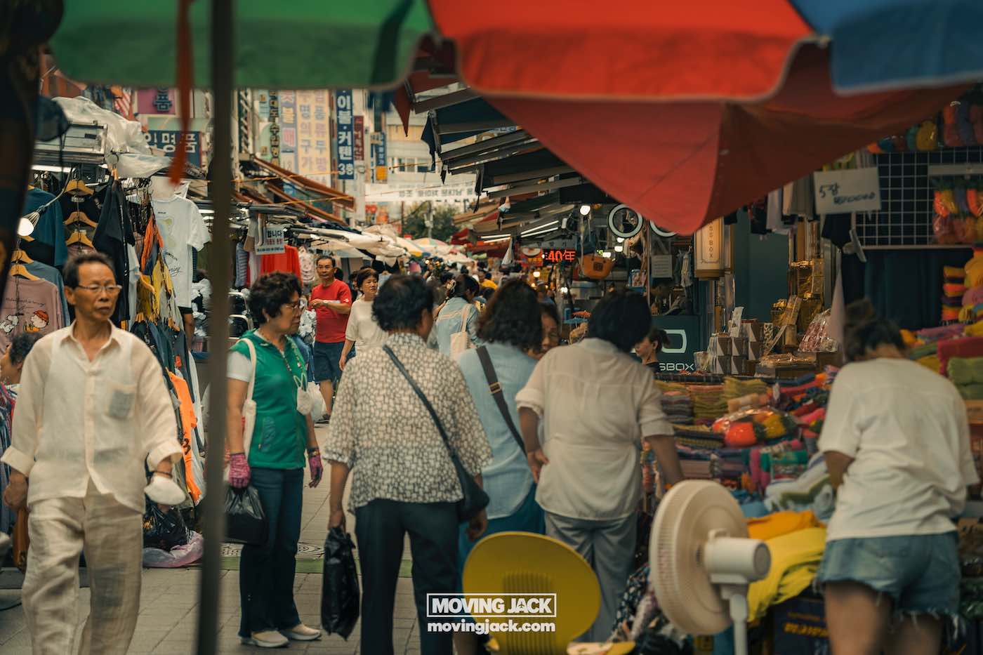 Wat te doen in Seoul: 13 unieke dingen om te doen + wat je beter kunt overslaan! 33 dingen om te doen in Seoul Mensen lopen door een drukke openluchtmarkt met kleurrijke paraplu's en verschillende kraampjes die kleding en goederen verkopen. -copyright-moving-jack. Com