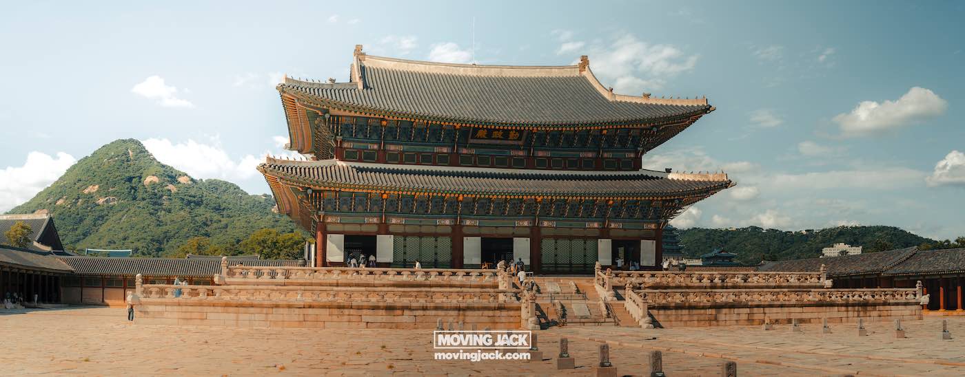Wat te doen in Seoul: 13 unieke dingen om te doen + wat je beter kunt overslaan! 4 dingen om te doen in Seoul Historisch paleisgebouw met sierlijke architectuur, tegen een bergachtige achtergrond onder een gedeeltelijk bewolkte lucht. -copyright-moving-jack. Com
