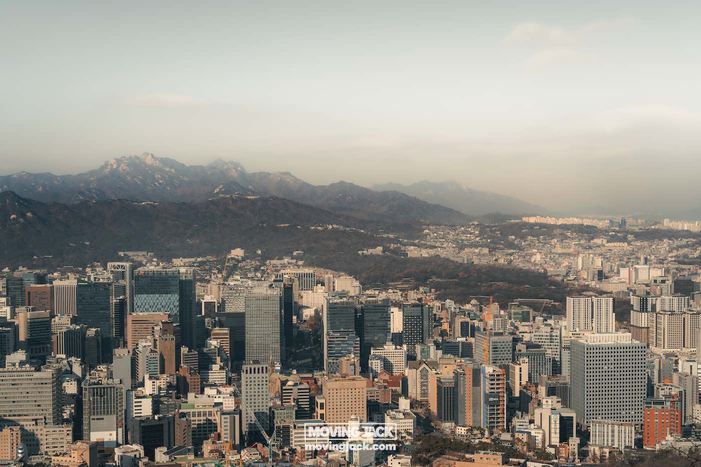 Wat te doen in Seoul: 13 unieke dingen om te doen + wat je beter kunt overslaan! 23 dingen om te doen in Seoul Luchtfoto van een stadsgezicht met talloze wolkenkrabbers en gebouwen, tegen een achtergrond van verre bergen onder een heldere hemel. -copyright-moving-jack. Com