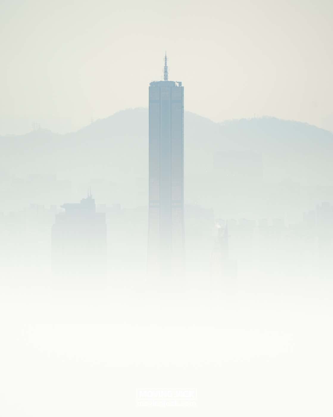 Wat te doen in Seoul: 13 unieke dingen om te doen + wat je beter kunt overslaan! 22 dingen om te doen in Seoul Een hoge wolkenkrabber komt uit dichte mist tevoorschijn, met vage contouren van omliggende structuren en heuvels op de achtergrond. -copyright-moving-jack. Com