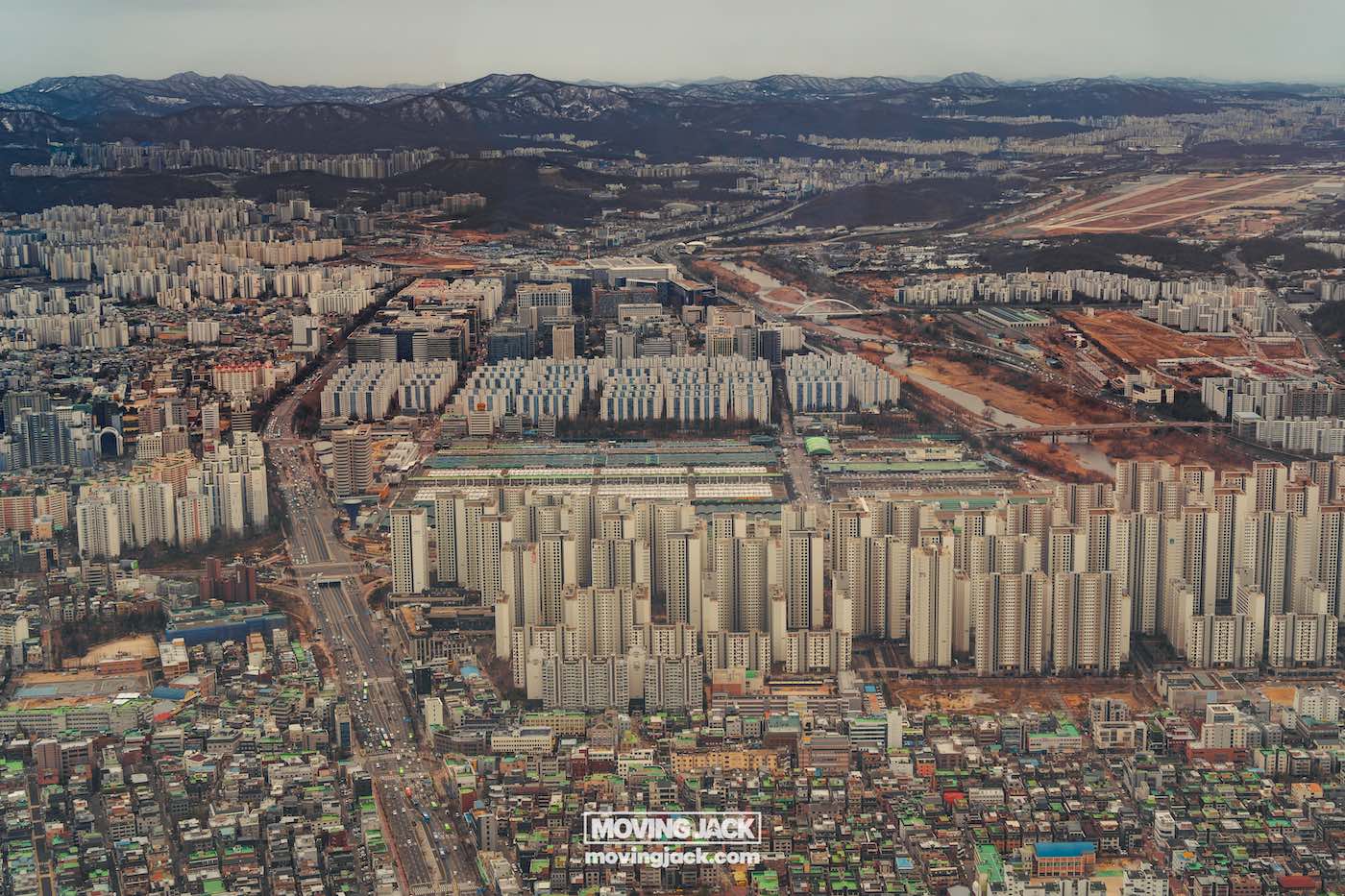 Wat te doen in Seoul: 13 unieke dingen om te doen + wat je beter kunt overslaan! 37 dingen om te doen in Seoul Luchtfoto van een dichtbevolkt stedelijk gebied met rijen hoge flatgebouwen, wegen en enkele open ruimtes. Bergen zijn zichtbaar op de achtergrond. -copyright-moving-jack. Com