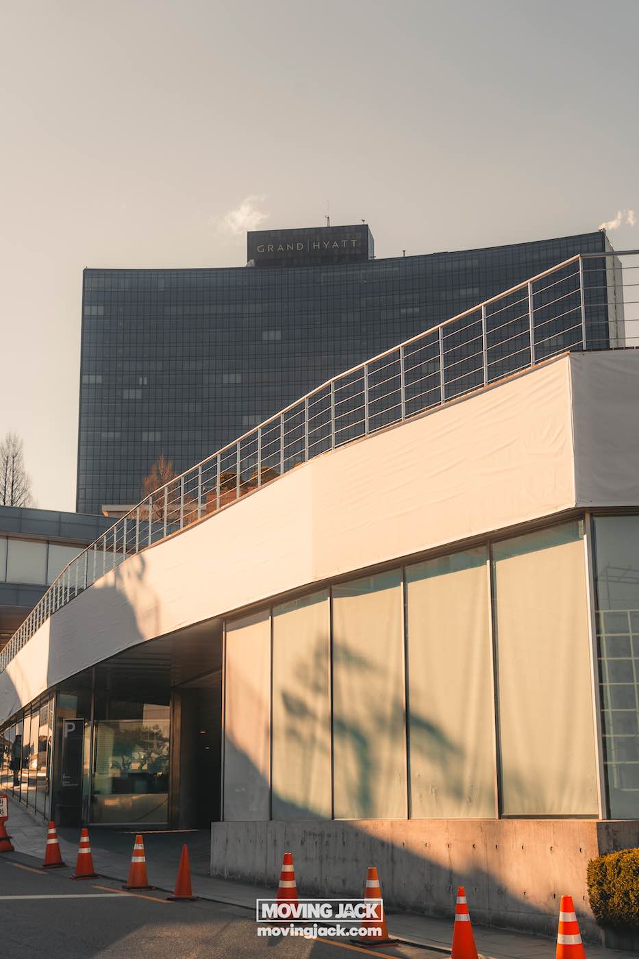 Reisroute Itaewon 2025: de beste eetgelegenheden, drankjes en uitgaansgelegenheden 16 Itaewon Uitzicht op een modern gebouw met een gebogen loopbrug aan de voorkant, oranje verkeerskegels langs de weg en een ander hoog gebouw met "grand hyatt" zichtbaar op de achtergrond. -copyright-moving-jack. Com