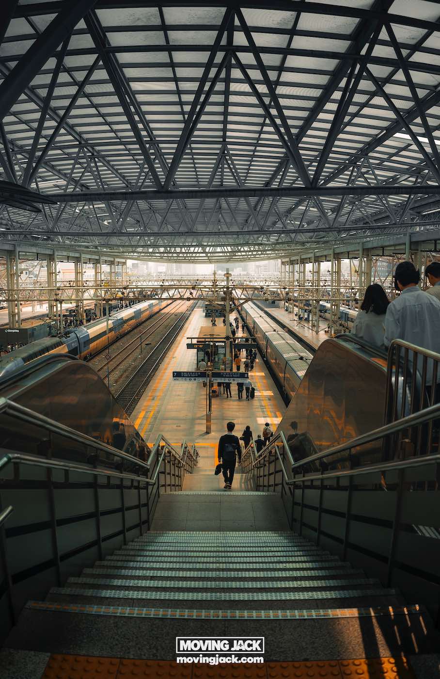 Gemakkelijk weekend in Busan met een peuter: 2-daagse reisroute voor gezinnen in Busan, weekend in Busan Uitzicht vanaf de bovenkant van een trap op een modern treinstation met verschillende perrons, treinen en mensen die lopen of wachten. -copyright-moving-jack.com