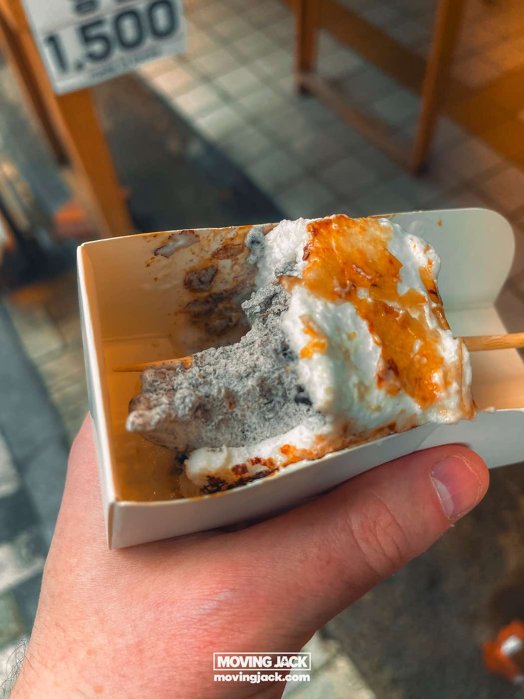 Gemakkelijk weekend in Busan met een peuter: 2-daagse reisroute voor gezinnen 25 Busan,weekend in Busan Een hand houdt een klein rechthoekig bakje vast met een half opgegeten dessert met een geroosterde, meringue-achtige topping en een houten stokje. -copyright-moving-jack.com