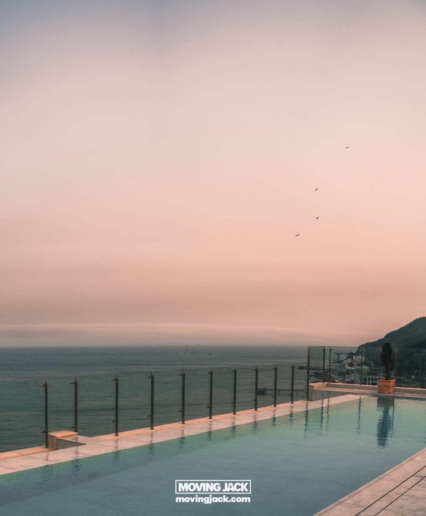 Gemakkelijk weekend in Busan met een peuter: 2-daagse reisroute voor gezinnen 7 Busan,weekend in Busan Een rustig infinity pool kijkt uit over de oceaan bij zonsondergang, met een glazen balustrade langs de rand en een kustlandschap in de verte. Vier vogels vliegen in de lucht. -copyright-moving-jack.com