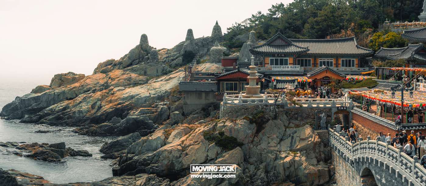 Gemakkelijk weekend in Busan met een peuter: 2-daagse reisroute voor gezinnen 26 Busan,weekend in Busan Traditioneel Koreaans tempelcomplex aan een rotsachtige kustlijn, met bezoekers die tussen gebouwen en lantaarns lopen, omringd door bomen en met uitzicht op de zee. -copyright-moving-jack.com