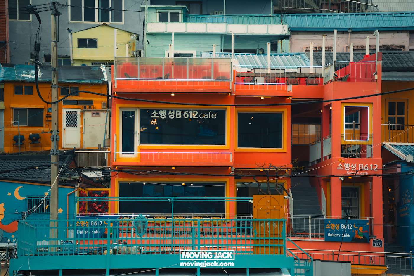 Gemakkelijk weekend in Busan met een peuter: 2-daagse reisroute voor gezinnen 10 Busan,weekend in Busan Een felgekleurd oranje en geel gebouw herbergt het b612 café, met grote ramen en bewegwijzering in het Koreaans, omringd door andere kleurrijke structuren. -copyright-moving-jack.com