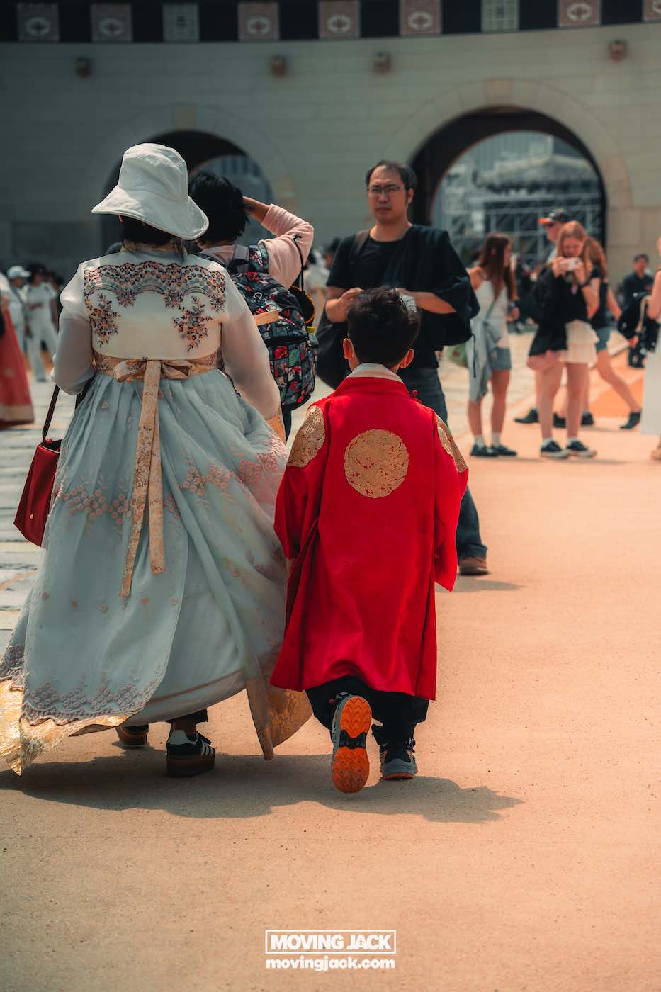Gyeongbokgung paleis Seoul ultieme gids + wandelvideo 16 Gyeongbokgung Een vrouw en een kind in traditionele Koreaanse hanbok lopen buiten bij Gyeongbokgung te midden van een groep informeel geklede mensen. -copyright-moving-jack.com