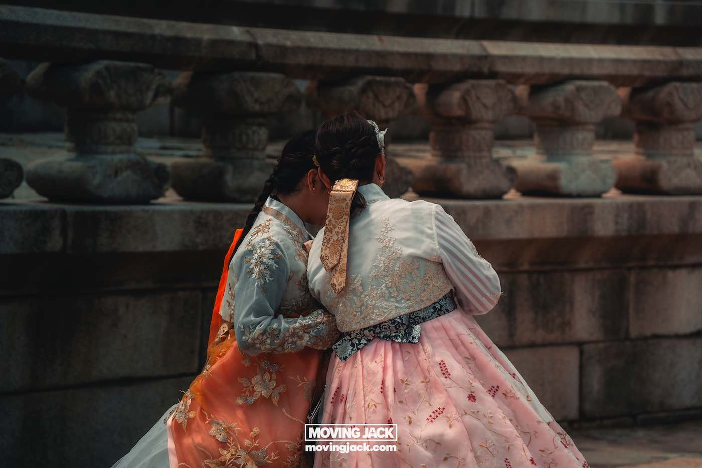 Gyeongbokgung paleis Seoul ultieme gids + wandelvideo 25 Gyeongbokgung Twee vrouwen, gekleed in traditionele Koreaanse hanbok, staan dicht bij elkaar bij een stenen balustrade en kijken uit over het terrein van het Gyeongbokgung-paleis. -copyright-moving-jack.com