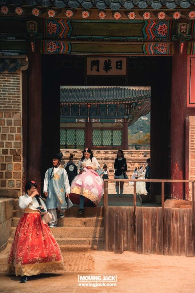Gyeongbokgung paleis Seoul ultieme gids + wandelvideo 4 Gyeongbokgung Mensen gekleed in traditionele Koreaanse hanbok lopen door de ingang van Gyeongbokgung, omringd door decoratieve patronen en prachtige houten architectuur. -copyright-moving-jack.com