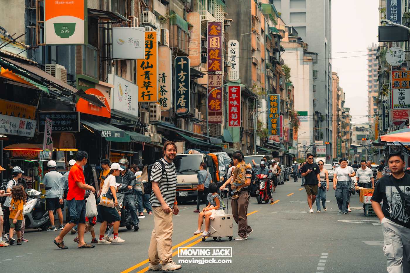 Reiscitaten: 120 unieke Instagram-bijschriften + generator voor 3 reiscitaten Levendige straat in een Aziatische stad, waar reiscitaten tot leven komen te midden van de drukte, scooters en levendige Chinese karakterborden langs de levendige winkelpuien aan beide kanten van de weg. -copyright-moving-jack.com
