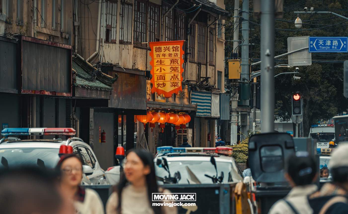Waar te verblijven in Shanghai: 5 leukste wijken + beste hotels 39 waar te verblijven in Shanghai Een drukke straat in een stedelijk gebied, perfect voor wie op zoek is naar een slaapplek in Shanghai, met voetgangers, politieauto's en rode Chinese lantaarns die buiten de winkels hangen. -copyright-moving-jack.com