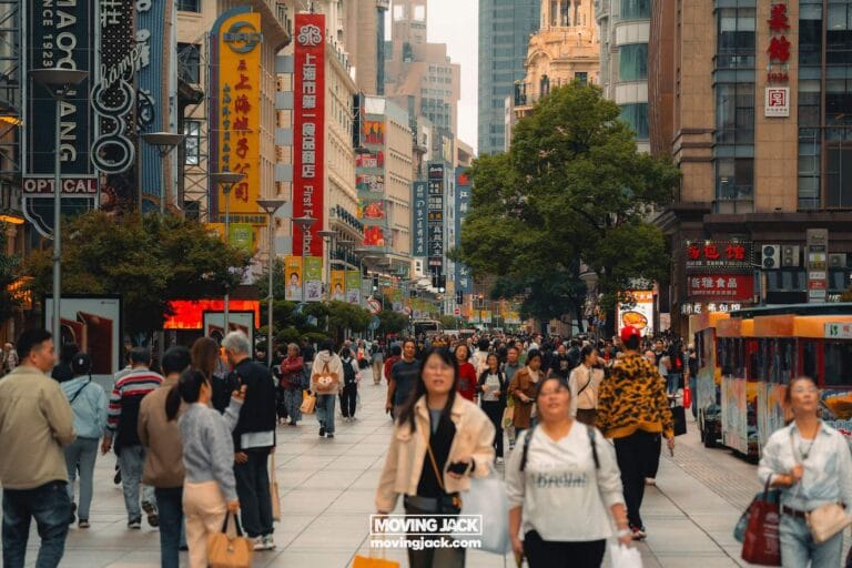 A busy urban street in shanghai with many people walking, tall buildings lined with colorful signs, and trees along the walkway—perfect for exploring while deciding where to stay in shanghai during the daytime. -copyright-moving-jack. Com