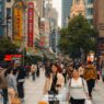 Where to stay in shanghai: 5 most fun areas + best hotels 21 travel quotes A busy urban street in shanghai with many people walking, tall buildings lined with colorful signs, and trees along the walkway—perfect for exploring while deciding where to stay in shanghai during the daytime. -copyright-moving-jack. Com