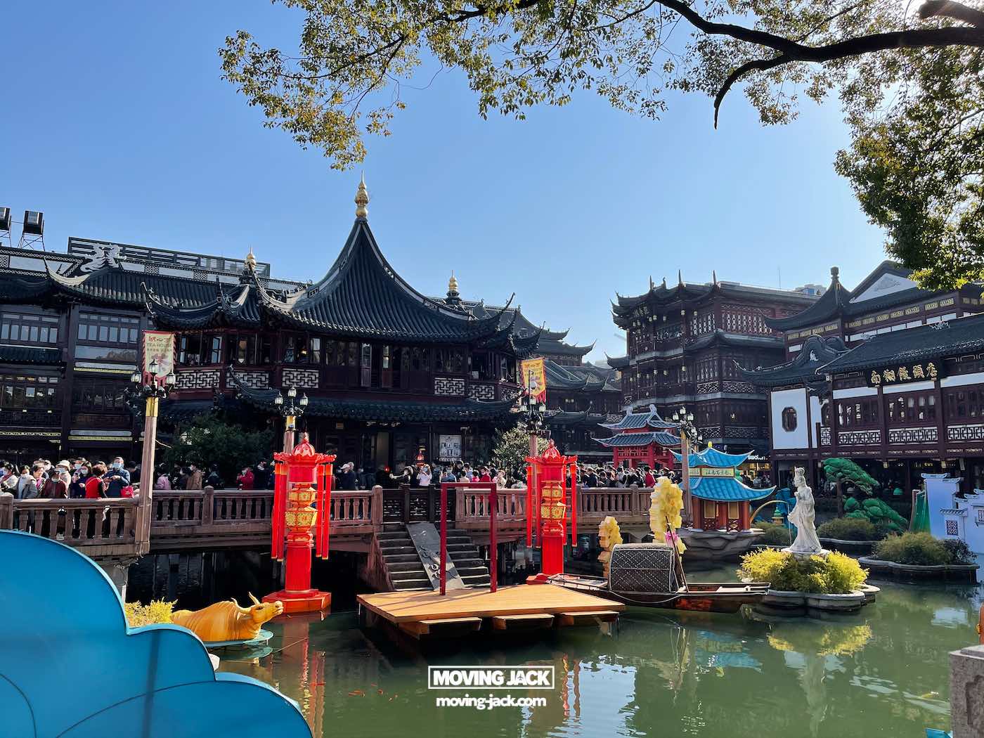 Is je tuin een bezoek waard in 2025? Complete gids & eerlijke lokale review: 5 dingen die je tuin een bezoek waard maken Traditionele Chinese architectuur omringt een vijver met rode lantaarns, beelden en een houten brug vol mensen onder een helderblauwe lucht. Hierdoor is uw tuin een bezoek waard vanwege de levendige sfeer en culturele schoonheid. -copyright-moving-jack.com