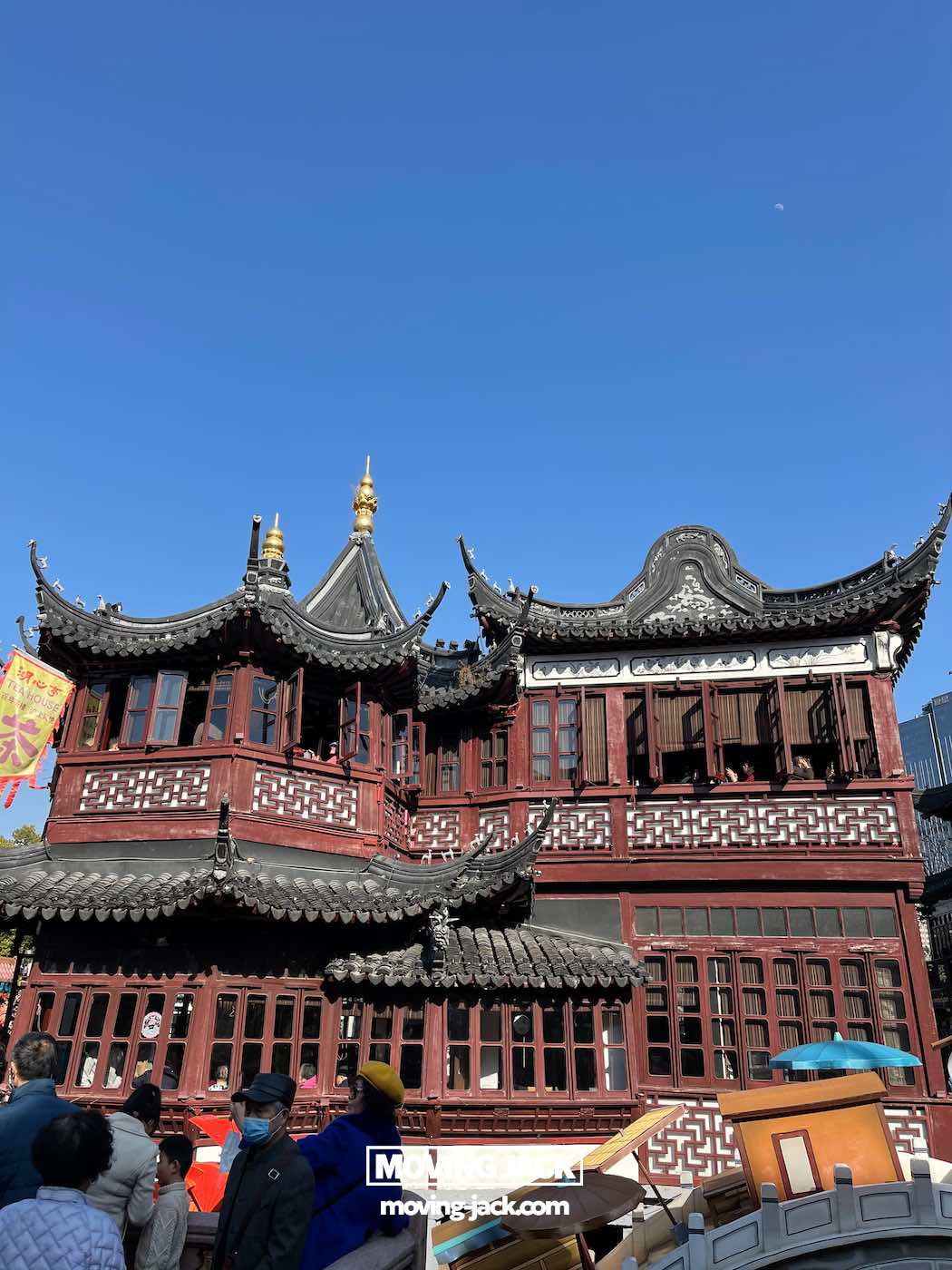 Is je tuin een bezoek waard in 2025? Complete gids & eerlijke lokale review 4 Is je tuin een bezoek waard? Een traditioneel Chinees gebouw met sierlijke gebogen daken en rode houten details staat onder een helderblauwe hemel in Yu Garden, een plek die een bezoek waard is. Er staan verschillende mensen vooraan. -copyright-moving-jack.com