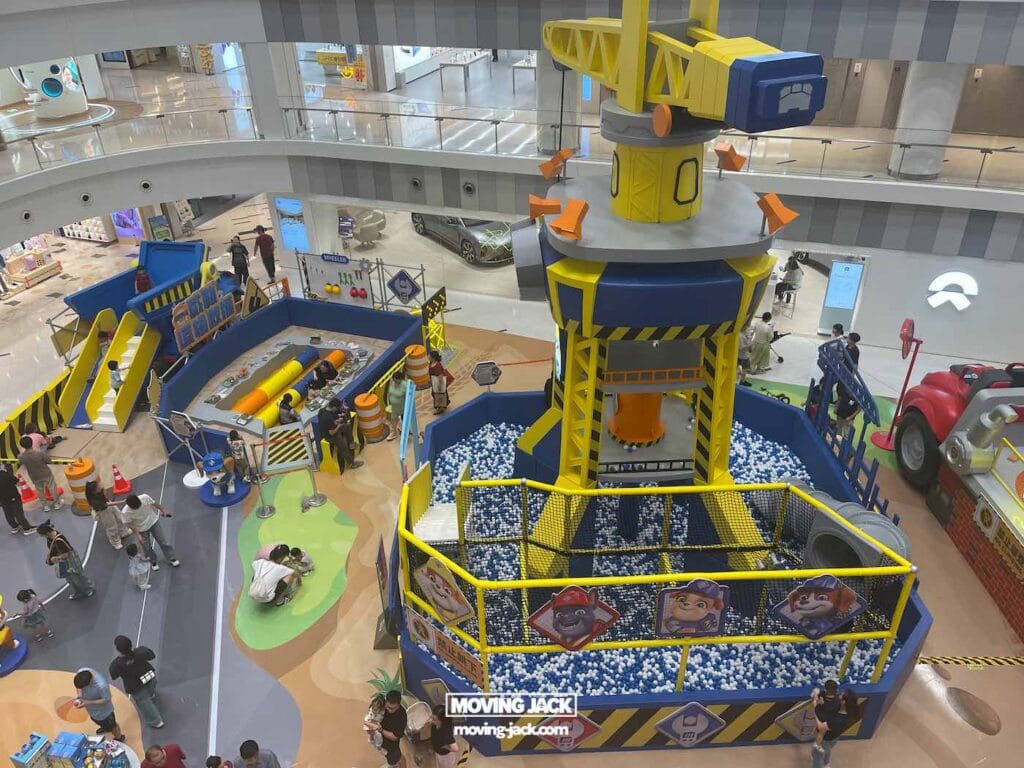 A construction-themed indoor play area with slides, a ball pit, and climbing structures, surrounded by children and adults in a shopping mall—perfect for families seeking fun things to do in Shanghai. -Copyright-moving-jack.com