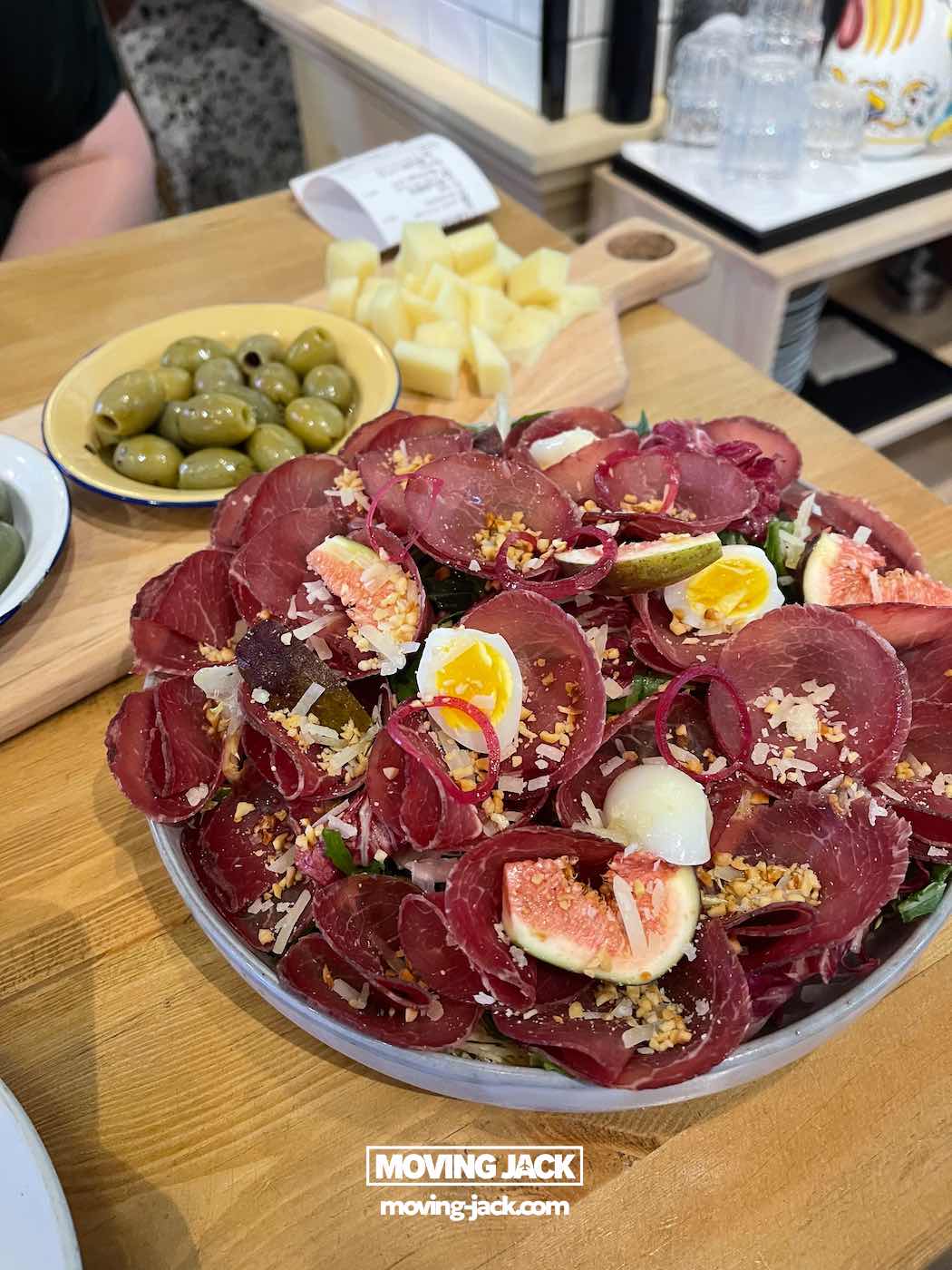 57 things to do in shanghai: the ultimate handbook 25 things to do in shanghai A salad with slices of cured meat, halved figs, boiled egg pieces, and grated cheese from alimentari restaurant, served alongside green olives and cubed cheese on a wooden table—showing delicious dining things to do in shanghai that capture the city's international food scene.