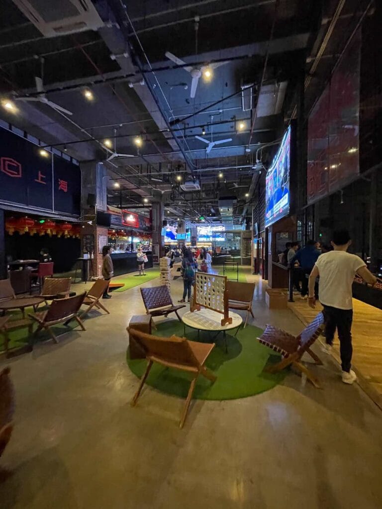 Shanghai 's nachts: beste handboek voor het nachtleven (2025) 15 Shanghai 's nachts Overdekt entertainmentgebied met zitplaatsen, kunstgras, lopende mensen en een grote vloer met vier verbindende spellen; gedempt licht en meerdere verlichte schermen boven het hoofd roepen de levendige energie van Shanghai bij nacht op. -copyright-moving-jack.com