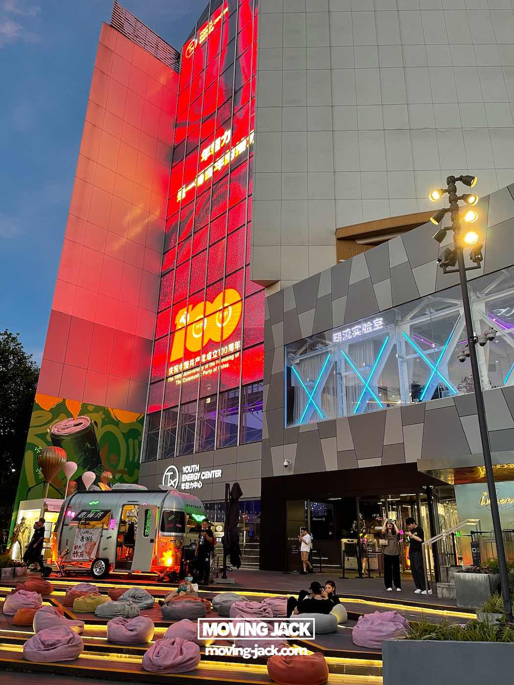 Shanghai 's nachts: beste handboek voor het nachtleven (2025) 8 Shanghai 's nachts Terras met zitzakken voor een modern gebouw, verlicht door neonlichten en grote digitale schermen – die doen denken aan Shanghai bij nacht – met een foodtruck die vlakbij geparkeerd staat. -copyright-moving-jack.com