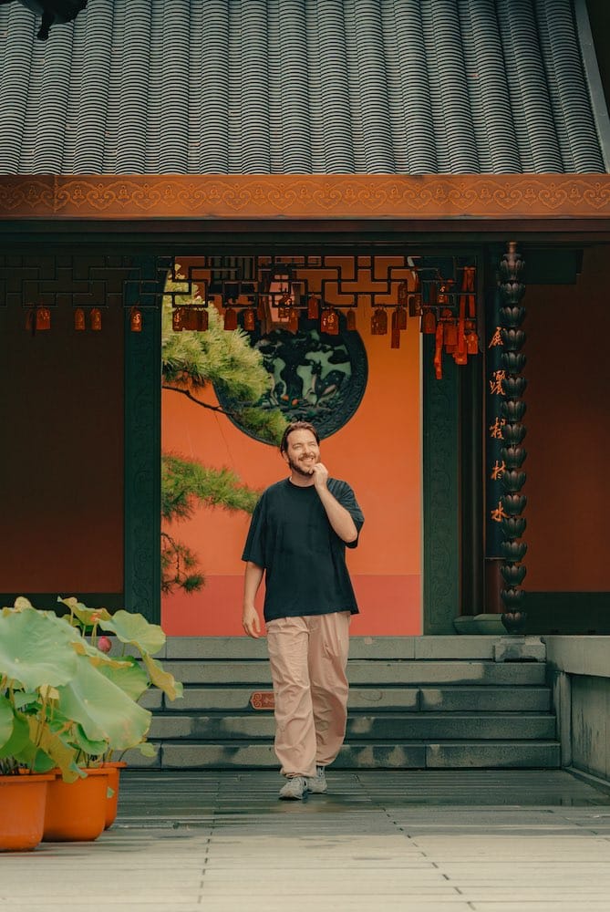 Waar te verblijven in Shanghai: 5 leukste wijken + beste hotels 43 waar te verblijven in Shanghai Een man in vrijetijdskleding loopt de trappen af voor een traditioneel gebouw met een oranje muur en hangende lantaarns. -copyright-moving-jack.com