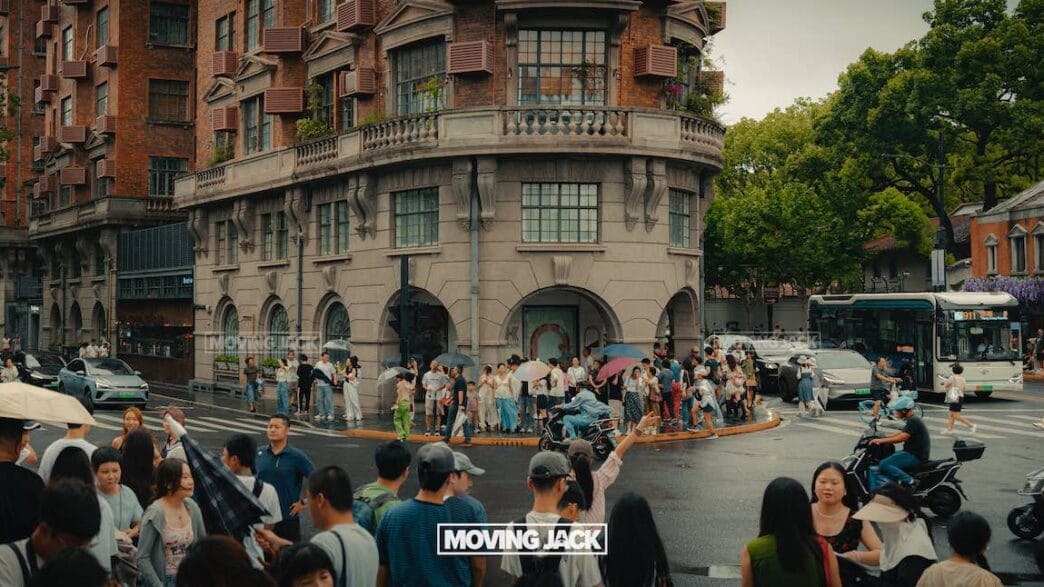 Crowded city intersection on a rainy day with people holding umbrellas and traffic; a historic building stands in the background. Discover everyday moments and things to do in shanghai. The words "moving jack" appear at the bottom center. -copyright-moving-jack. Com