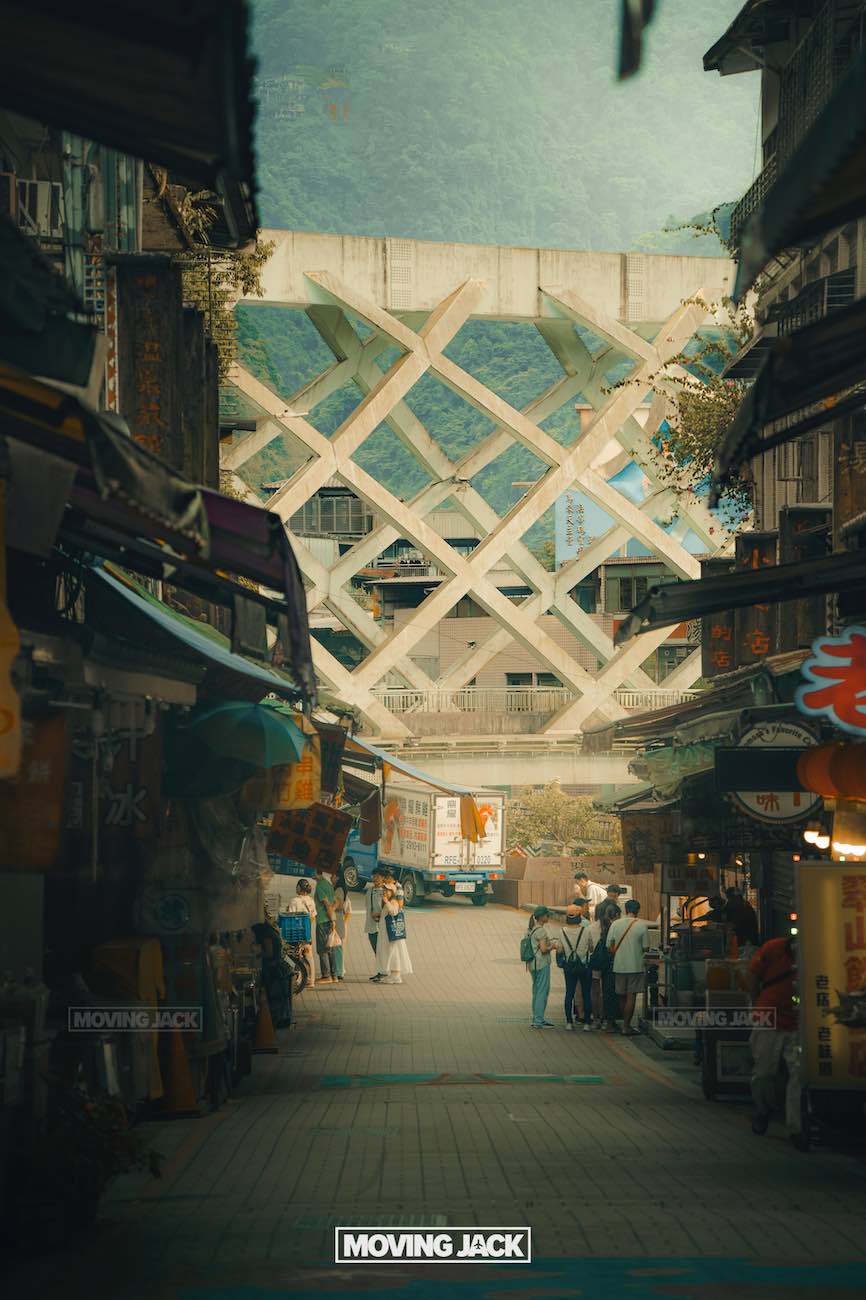 20+ best things to do in taipei (by an expert) 35 things to do in taipei A narrow urban street lined with shops leads to a large, geometric concrete bridge—one of the best things to do in taipei. People walk and gather nearby, while mountains rise in the distance and a truck is parked near the bridge. -copyright-moving-jack. Com