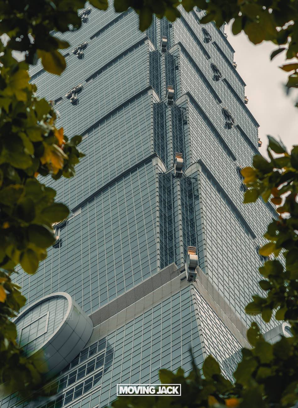 20+ best things to do in taipei (by an expert) 8 things to do in taipei A close-up view of the glass facade of taipei 101 skyscraper, framed by leafy tree branches, with the "moving jack" logo at the bottom center of the image. -copyright-moving-jack. Com
